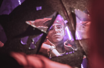Rap-artisti Ale katsoo kameraa kohti lasinsirpaleen kautta.