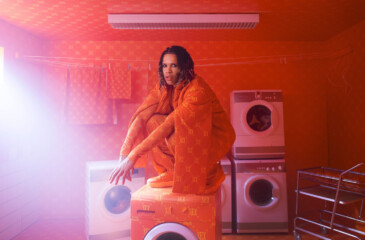 Sexmane istuu pesukoneen päällä oranssissa huoneessa.