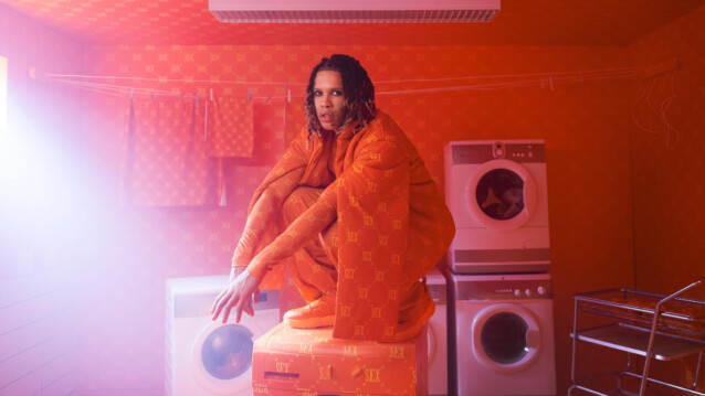 Sexmane istuu pesukoneen päällä oranssissa huoneessa.