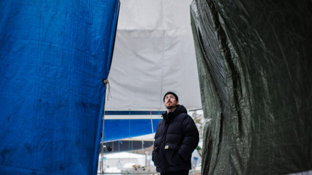 DJ Kridlokk seisoo pressuilla päällystettyjen laivojen välissä.