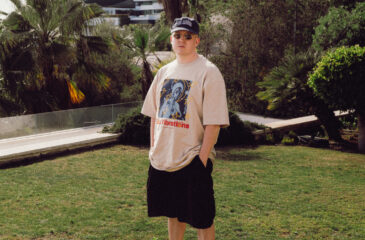 Lyttä seisoo trooppisessa puutarhassa, päällään kuvitettu t-paita, edustamassa Def Jam Recordings Finland -levy-yhtiötä.