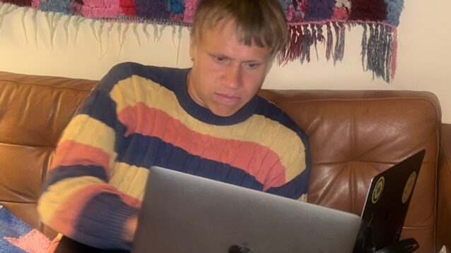 Räppäri AB kuvattuna sohvalla kahden tietokoneen kanssa, päällään raidallinen villapaita. Klangin haastattelu pyrkii selvittämään vastauksen kysymykseen: Kuka on AB?