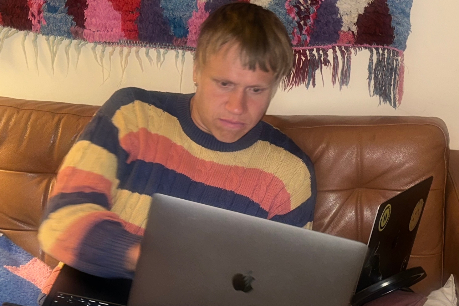 Räppäri AB kuvattuna sohvalla kahden tietokoneen kanssa, päällään raidallinen villapaita. Klangin haastattelu pyrkii selvittämään vastauksen kysymykseen: Kuka on AB?