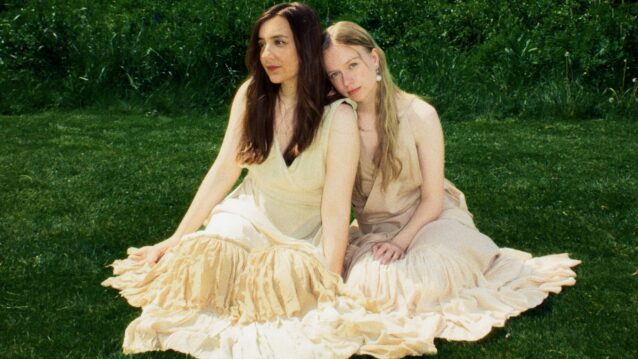 Emma & Matilda nurmikolla istumassa. Emma & Matilda esiintyvät Yle Kesäfestivaali 2026 -tapahtumassa!