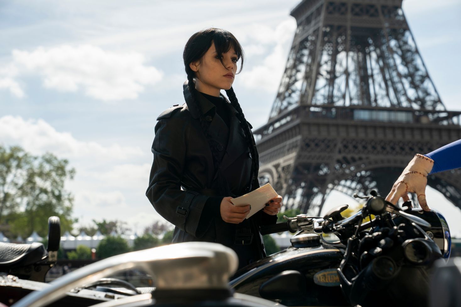 Jenna Ortega Wednesday Addamsina Eiffel-tornin edessä, Thing-käsi moottoripyörän ohjaustangolla