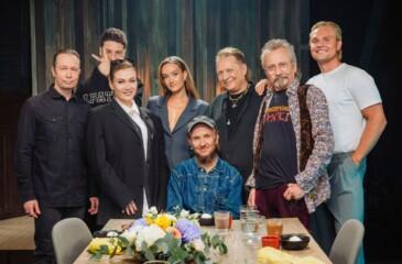 Samuli Putron Vain elämää -jakson artistit poseeraavat kukkakoristellun pöydän ääressä studiossa.