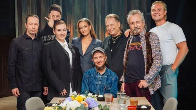 Samuli Putron Vain elämää -jakson artistit poseeraavat kukkakoristellun pöydän ääressä studiossa.